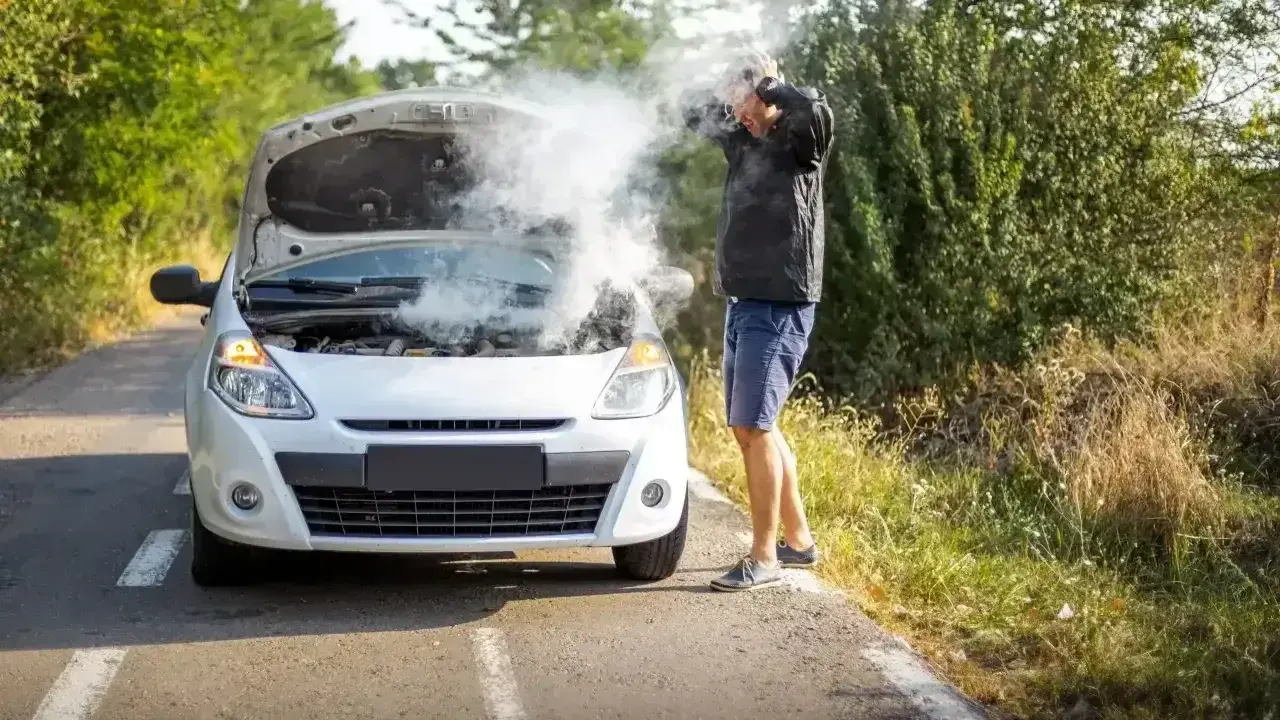 Mężczyzna z rozpaczą w rękach przy samochodzie z dymiącym silnikiem. Rozbiegany diesel na poboczu drogi.