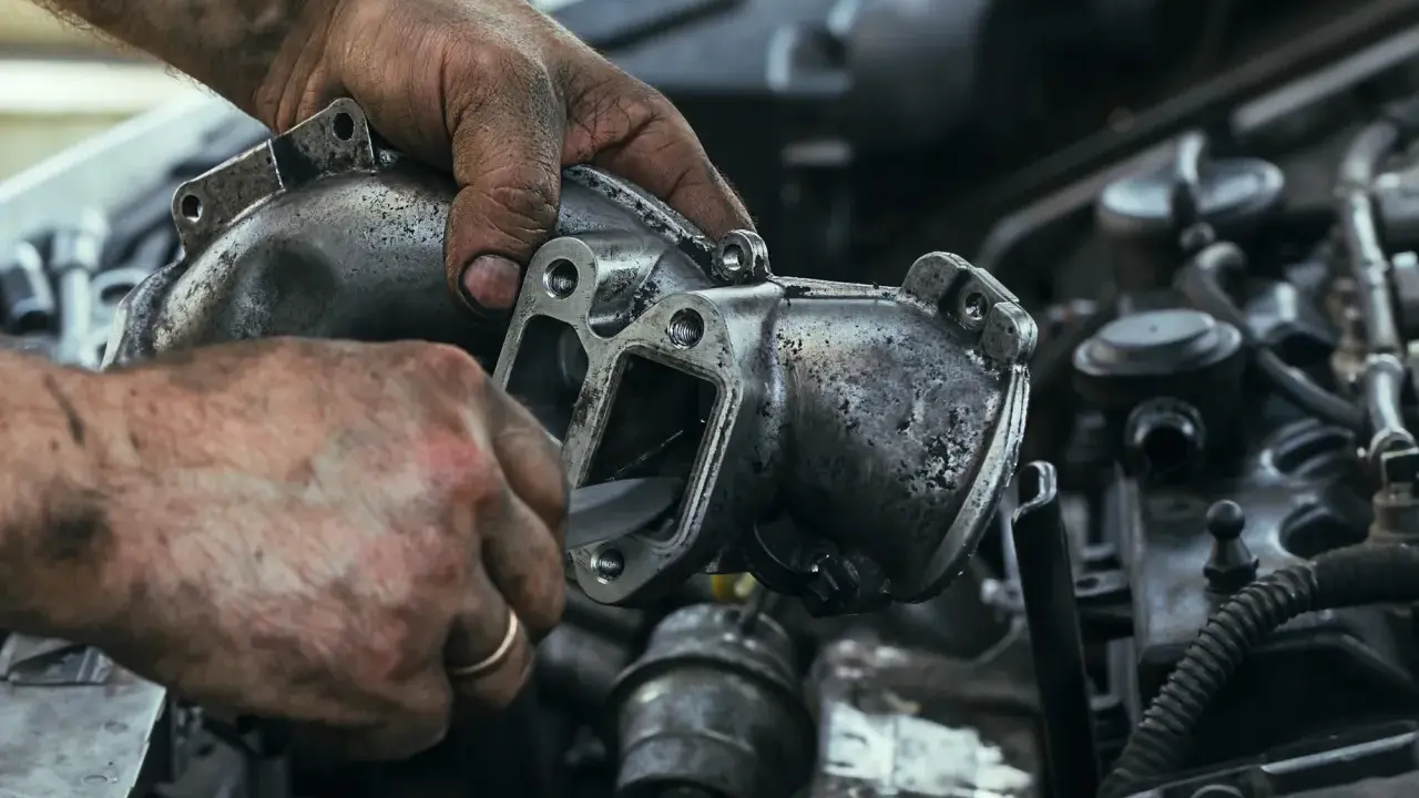 Brudne ręce mechanika czyszczą zapieczony zawór EGR. Widać narzędzie wsuwane do wnętrza elementu.