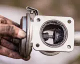 Brudny zawór EGR, z widocznym nagarem wewnątrz. Ręka mechanika trzyma element.