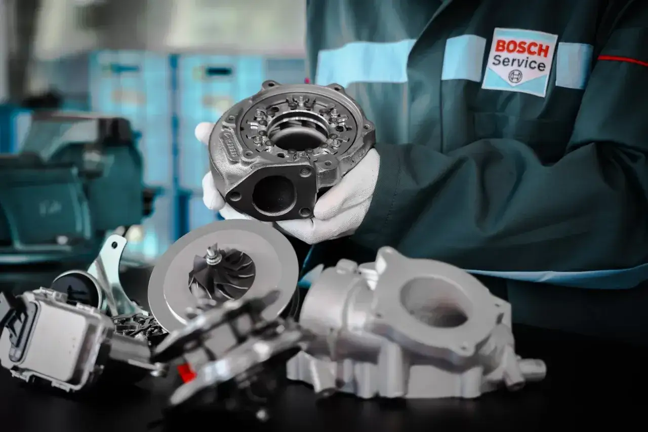 Mechanik w fartuchu Bosch Service pokazuje części turbosprężarki, kluczowe do tego, jak sprawdzić turbinę.
