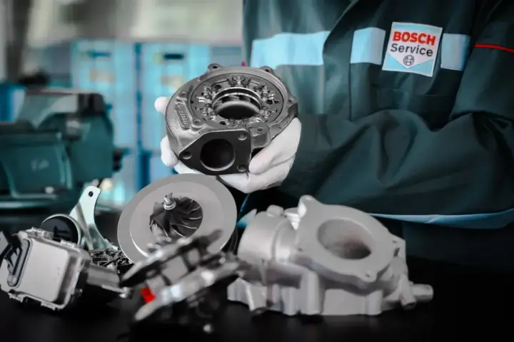 Mechanik w rękawiczkach prezentuje turbosprężarkę do silnika diesla, obok leżą jej części.